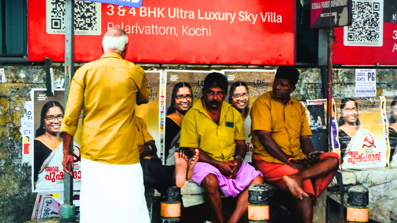 A group of auto drivers seen in Kochi, Kerala ahead of the 2026 Assembly Elections. On the wall behind them, posters of candidate Advocate Pushpa Das can be seen.