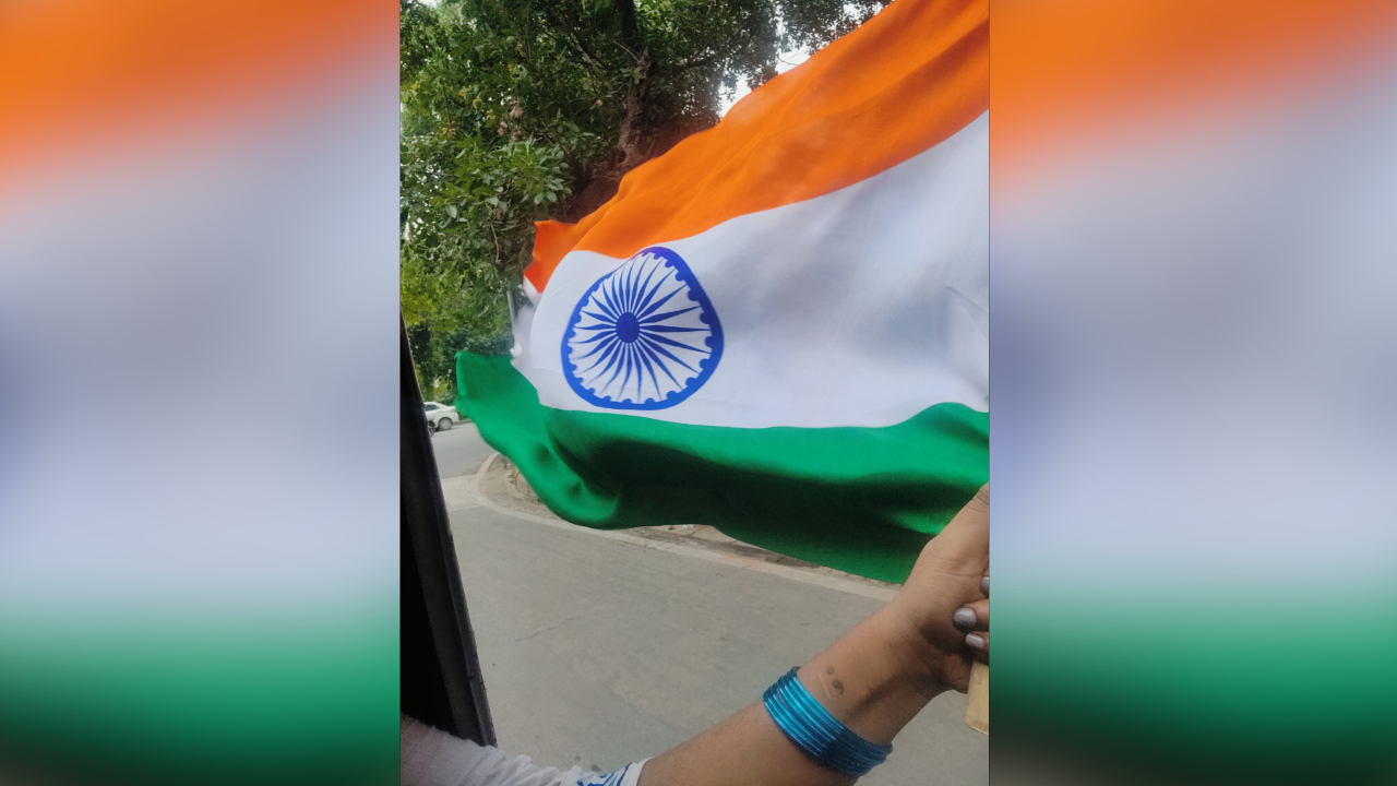 A woman's hand with bangles can be seen holding the Indian flag. She is travelling in an auto.